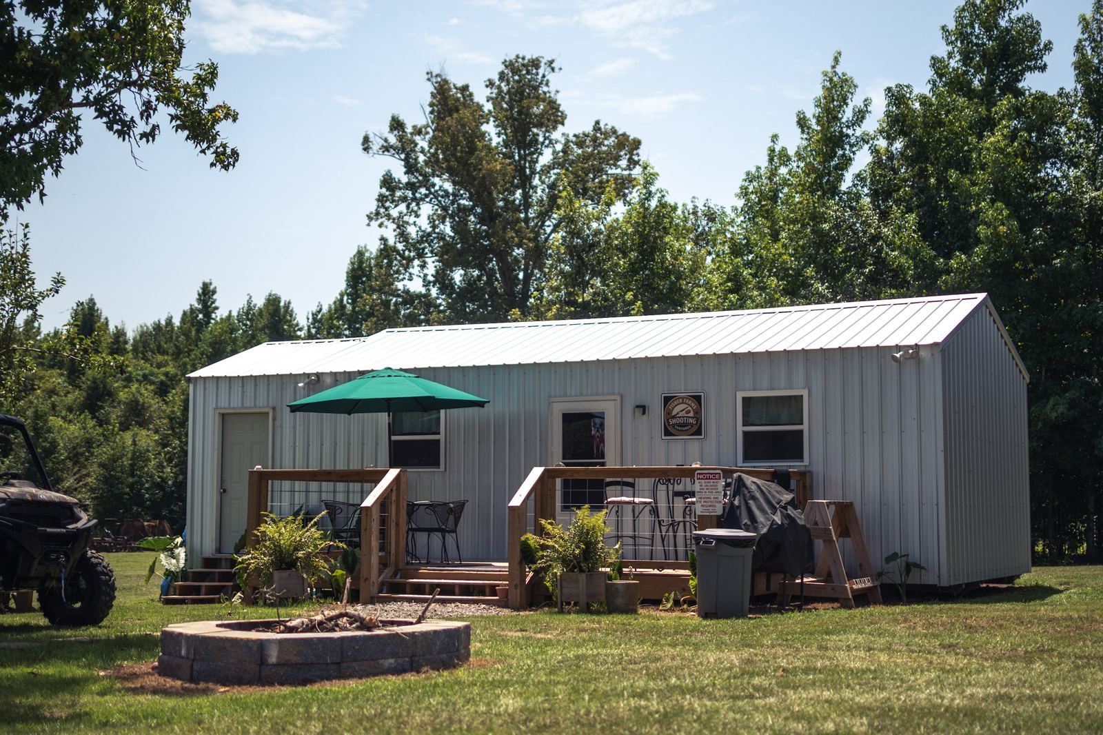 The clubhouse at Fisher Farms Shooting Ventures, a white metal building with a covered deck, green umbrella, seating and a fire pit out front